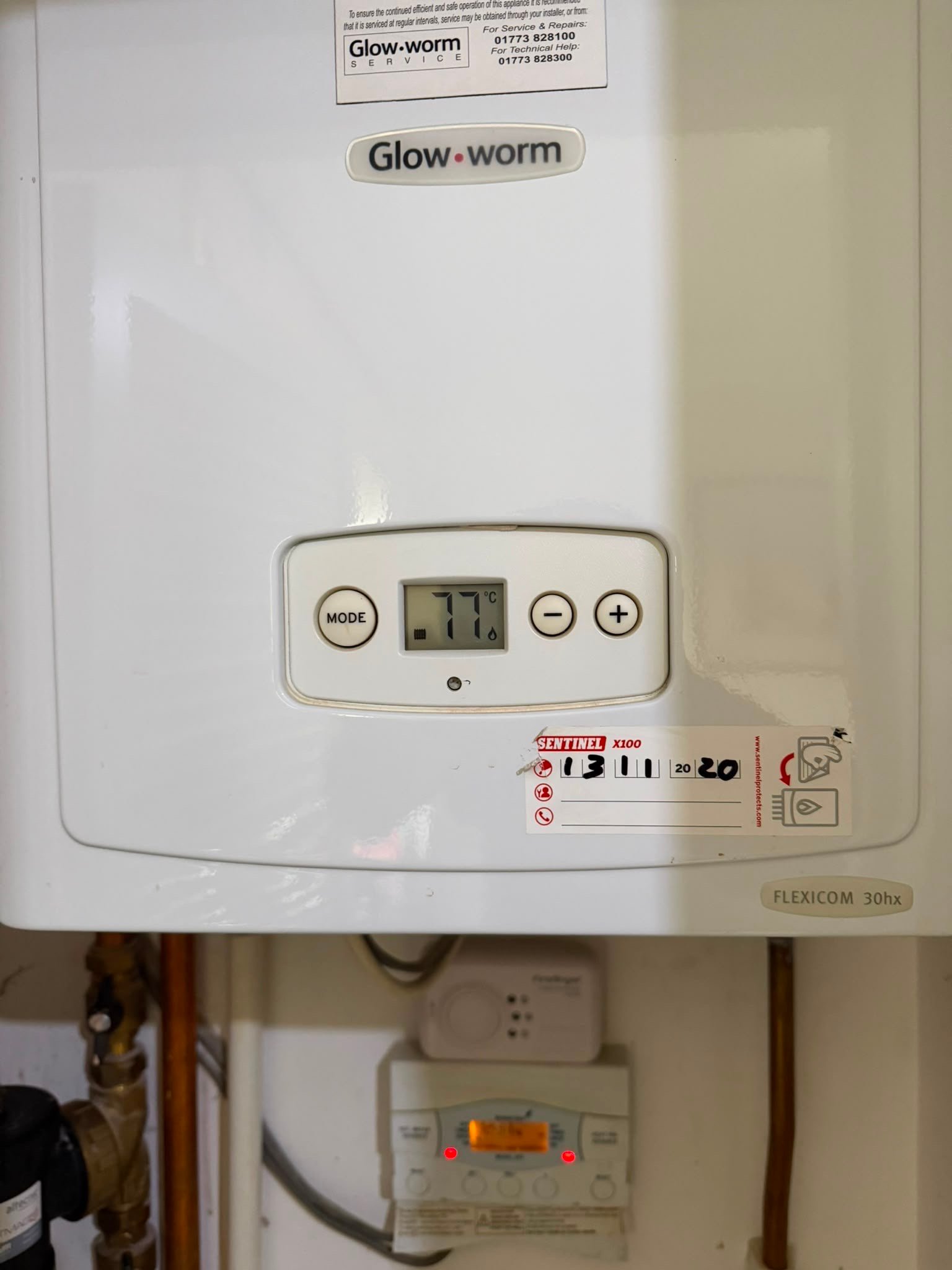 Close-up of a modern white Glow-worm Sentinel X100 gas boiler displaying a temperature of 77