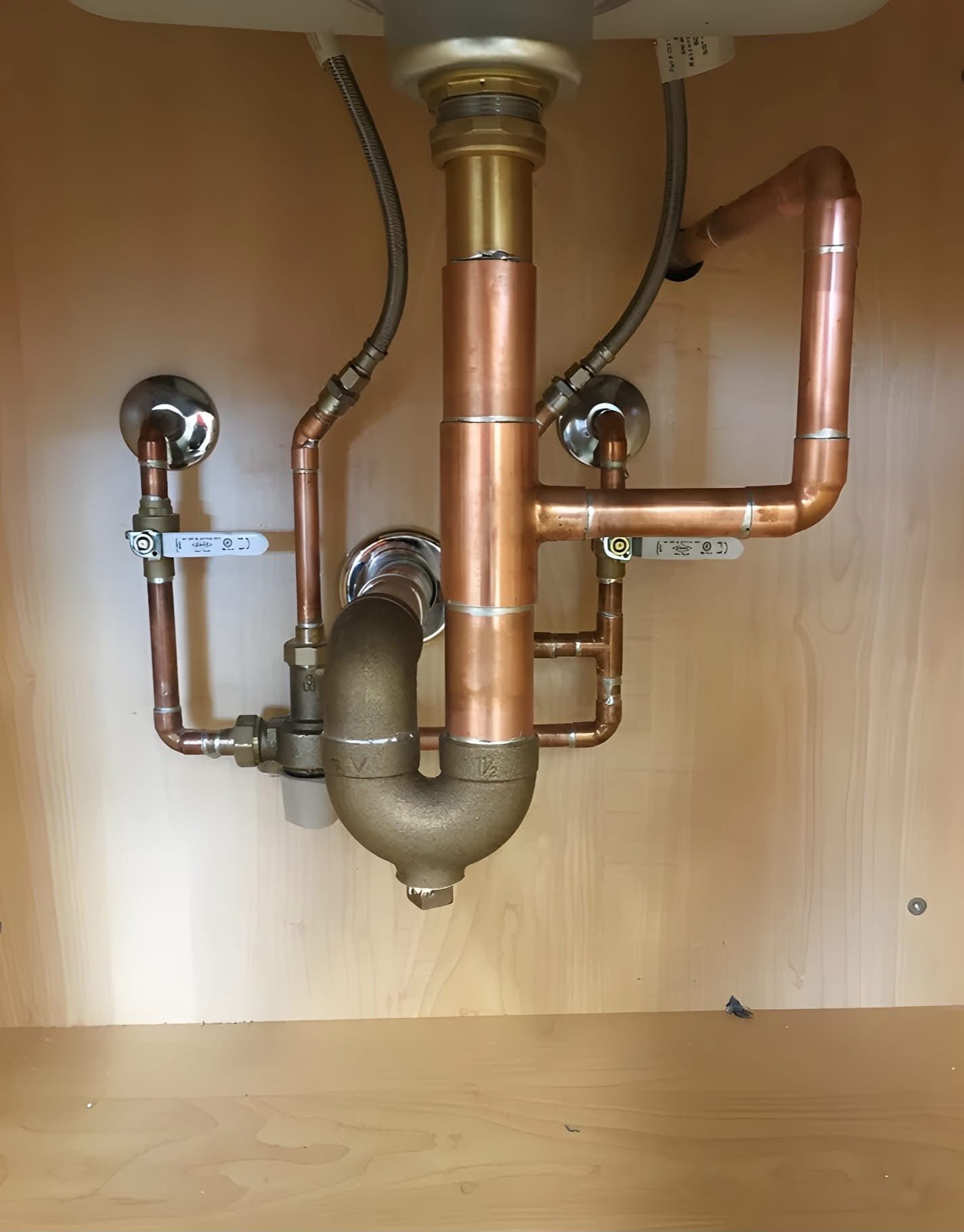 Close-up view of intricate copper plumbing pipes and fittings beneath a sink, showcasing KOZ Plumbing