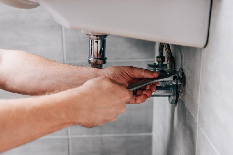 Plumber using wrench to repair a bathroom sink tap, showcasing KOZ Plumbing & Heating's bathroom
