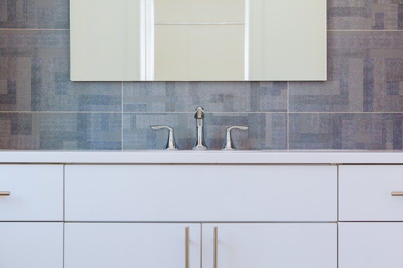 Close-up of a modern bathroom vanity with chrome taps and a grey tiled wall, showcasing