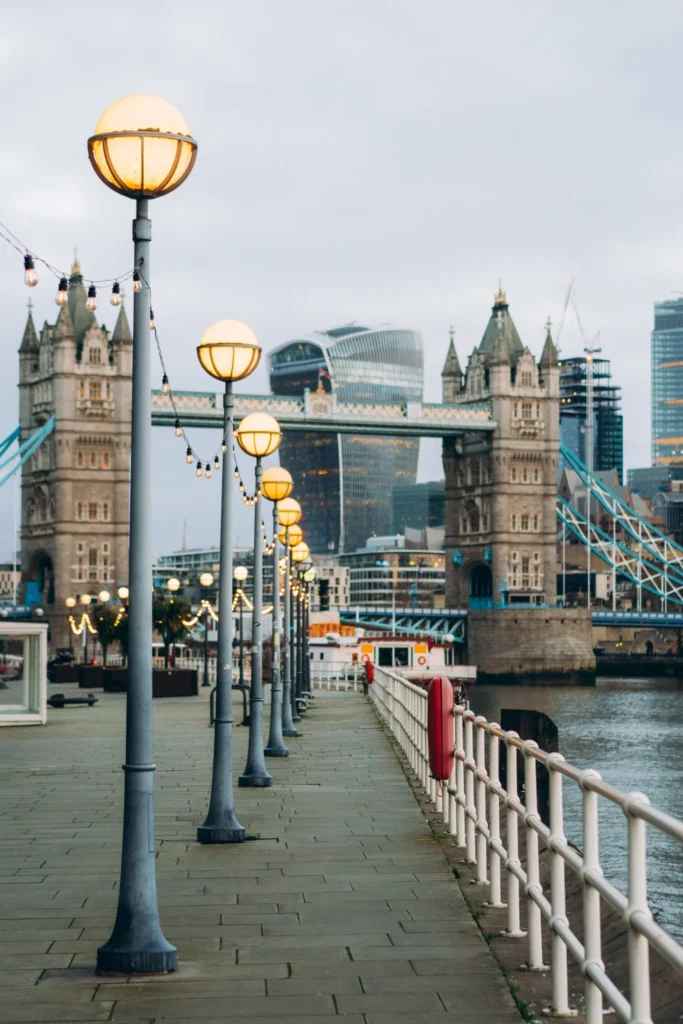 A row of London street lamps lines a walkway with Tower Bridge and city skyline