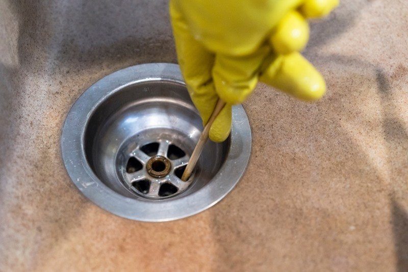 Hand in yellow glove clearing a blocked sink drain, demonstrating KOZ Plumbing & Heating’s drain