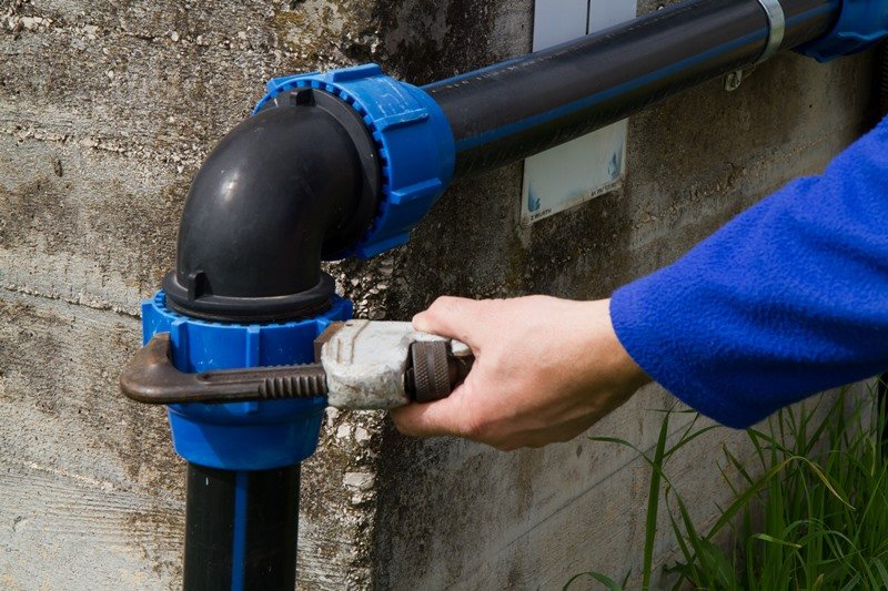 Close-up of a plumber's hand using a wrench to tighten a blue plastic pipe fitting,