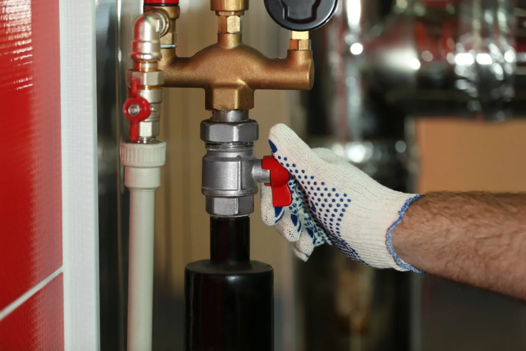 Hand in a protective glove turning a valve on a heating system, representing boiler repairs