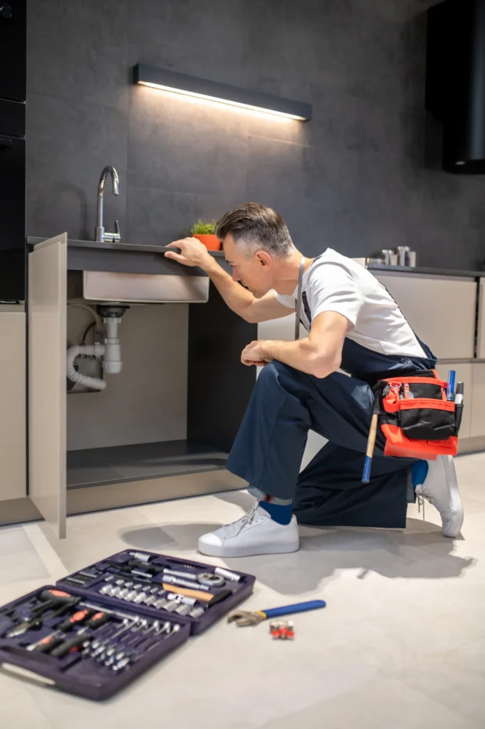 Plumber kneeling and inspecting pipes under a sink, demonstrating 24/7 emergency plumbing services across Essex for KOZ Plumbing & Heating.
