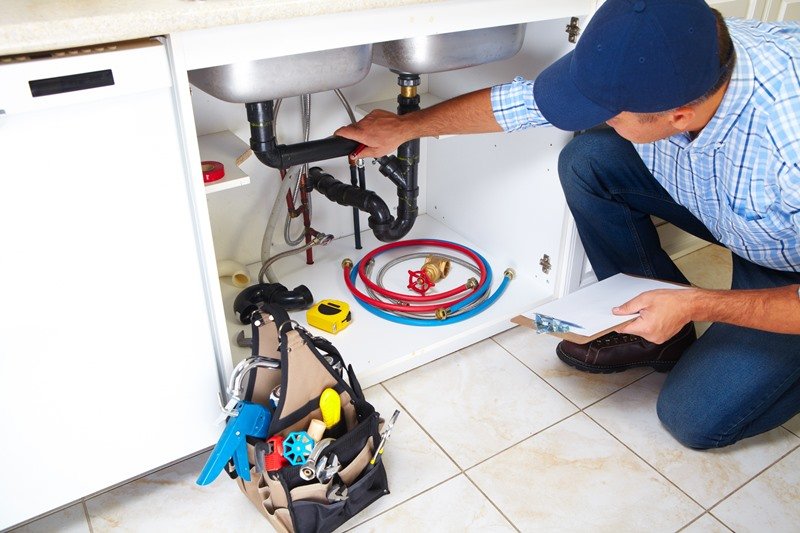 KOZ Plumbing & Heating technician working on a sink drain under a kitchen cabinet, demonstrating
