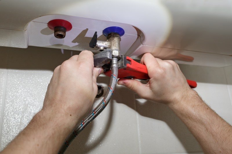Plumber using pliers to repair a boiler pipe connection, demonstrating KOZ Plumbing & Heating’s expertise