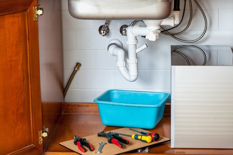 Close-up view of a kitchen sink plumbing setup with pipes and tools, illustrating general plumbing