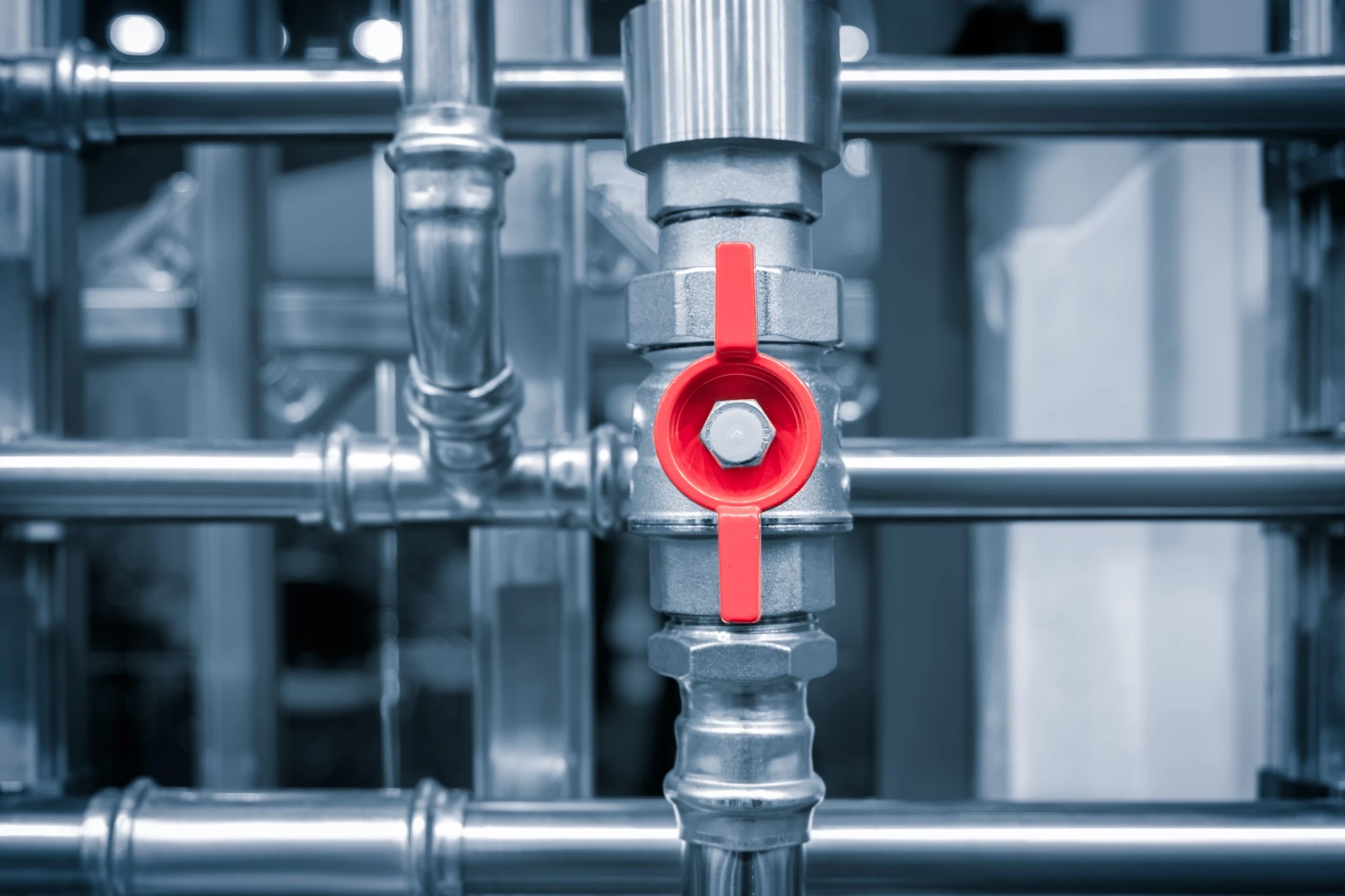 Close-up of a complex plumbing system in a boiler room, featuring metal pipes, valves, and